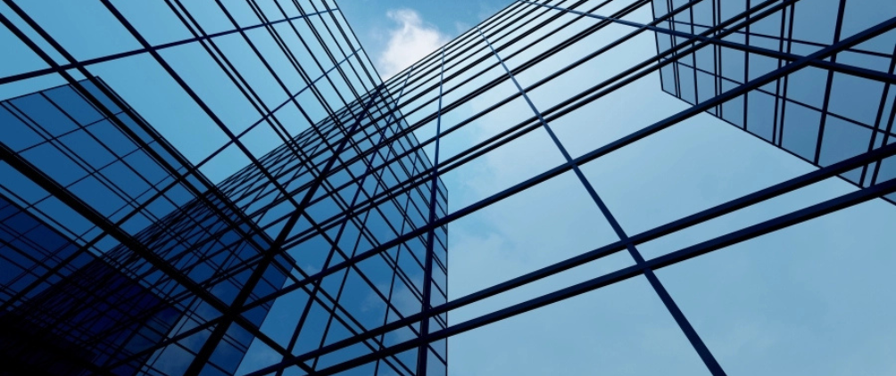 Upward view of modern glass skyscrapers reflecting the blue sky and clouds, creating a geometric pattern of lines and reflections.