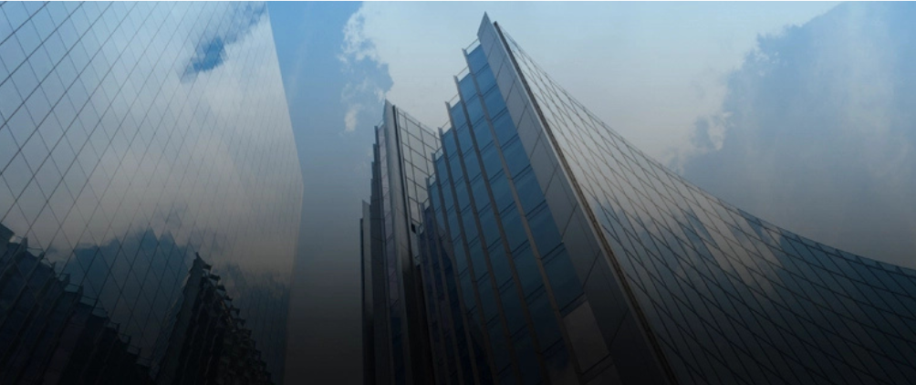 Tall modern glass skyscrapers reflecting the cloudy sky, viewed from a low angle.
