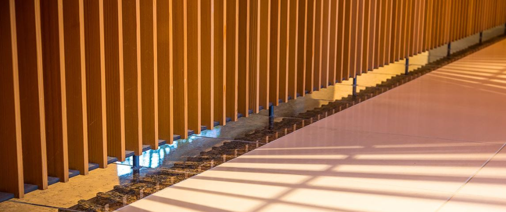 Close-up of modern architectural wooden slats casting geometric shadows on a polished marble and tile floor, highlighting warm lighting and contemporary interior design elements.