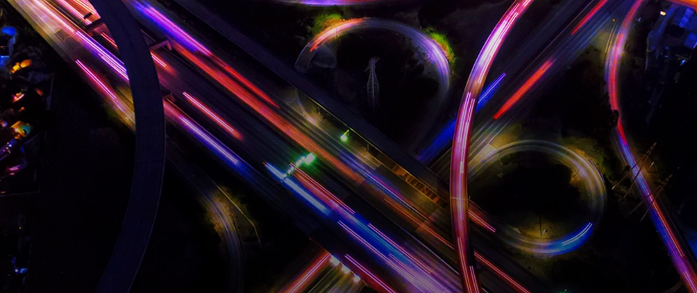 Aerial view of a highway interchange at night with colorful light trails representing leveraged finance, market complexity and the AI credit divide.