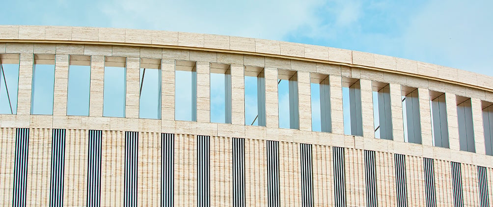 Curved facade of a modern building with tall windows against a blue sky.