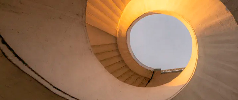 Spiral concrete staircase illuminated by warm sunlight.