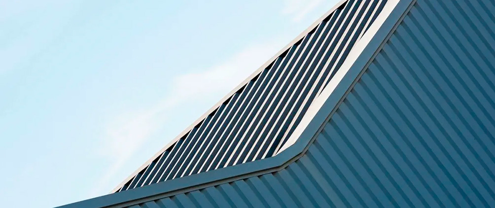 Abstract close-up of a modern metal roof with diagonal black slats against a pale blue sky.