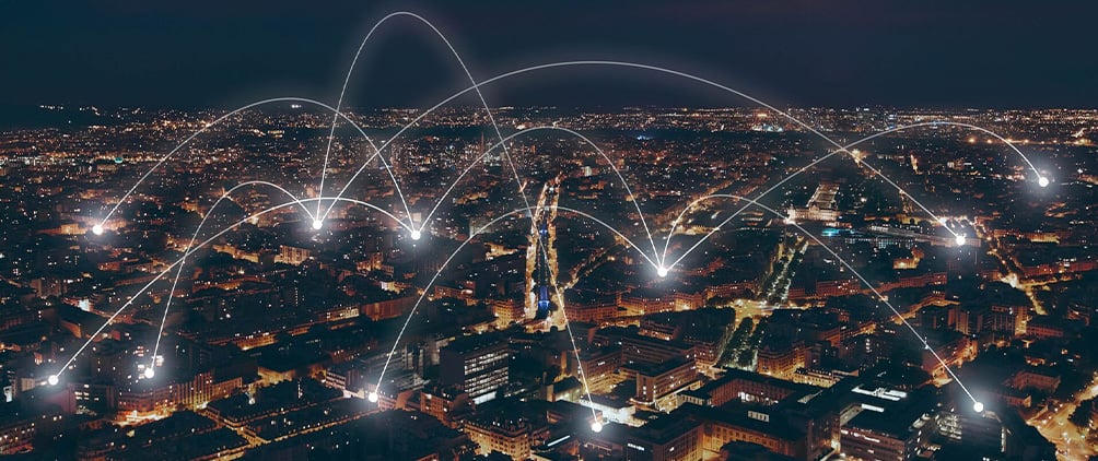 Nighttime aerial view of a city with illuminated arcs connecting locations, representing global markets and investment opportunities.