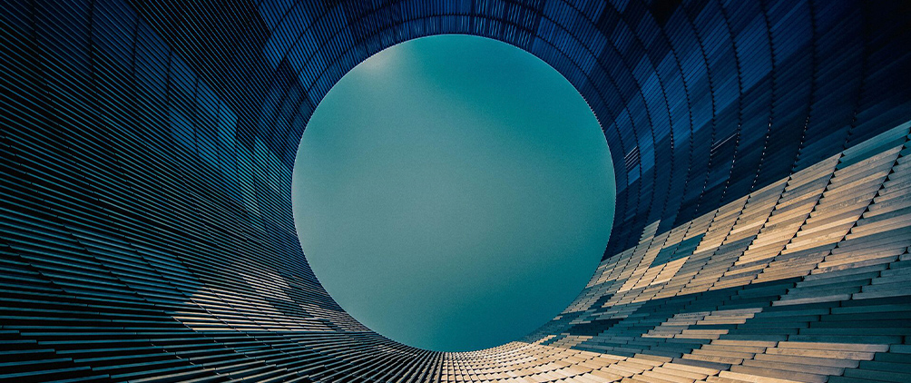 Circular architectural structure with a teal opening and layered geometric panels.