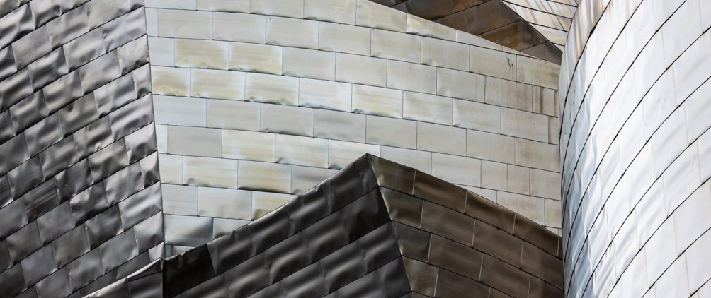 Close-up of curved, overlapping metallic building panels in shades of silver and gray