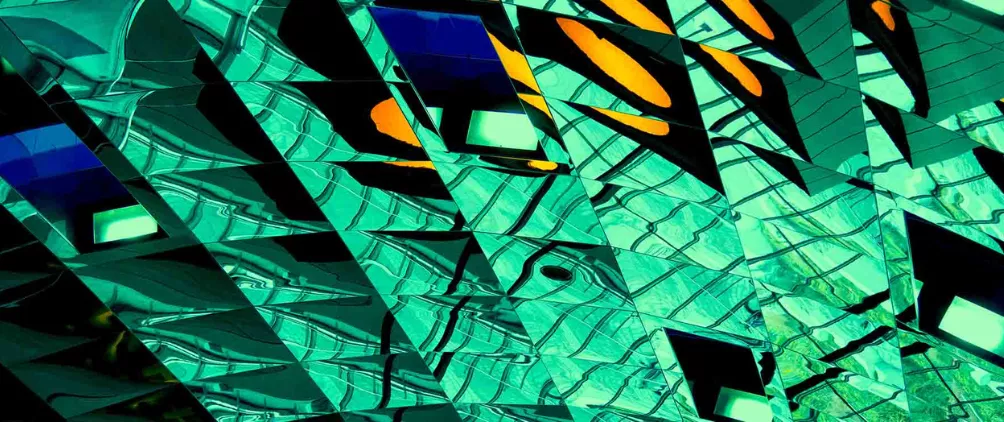 Abstract geometric pattern of reflective glass surfaces with teal, yellow, and black shapes creating a modern, futuristic architectural design.