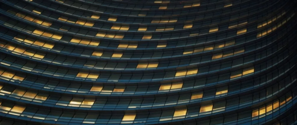Curved modern office building at night with rows of illuminated windows creating a wave-like architectural pattern.