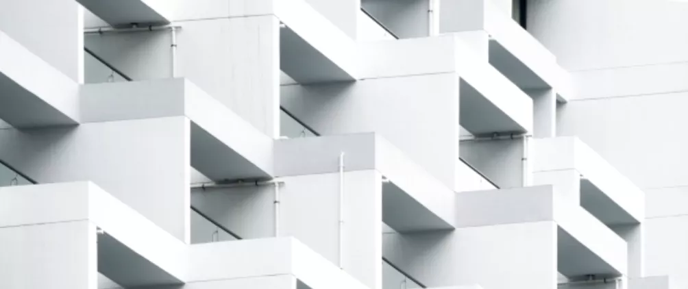 Modern white geometric apartment building with repeating angular balconies creating a minimalist architectural pattern.