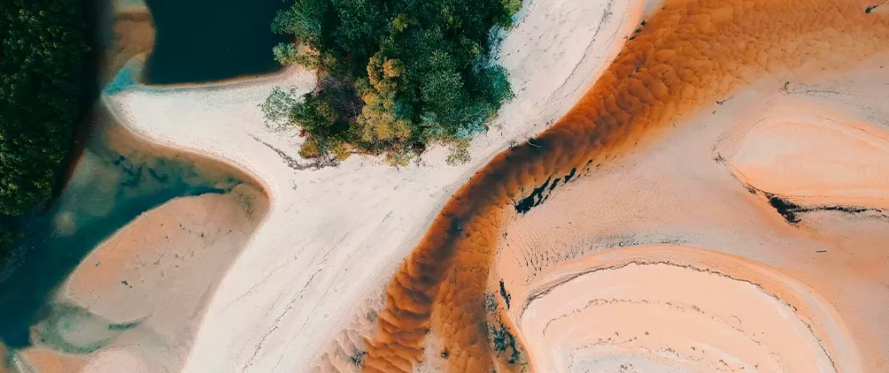 Aerial view of winding shoreline and sand formations representing changing market conditions and investment outlook.